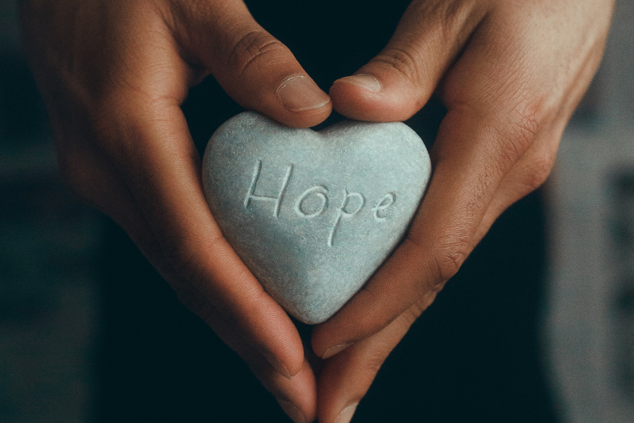 Stock image of hands holding a heart-shaped stone with the word "Hope" carved into it