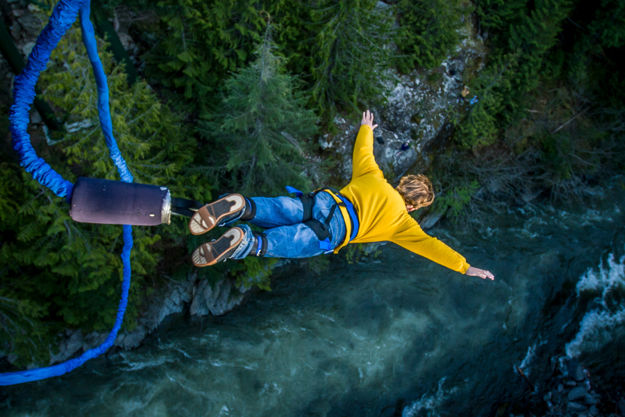 Man in yellow shirt bungee jumping into a canyon