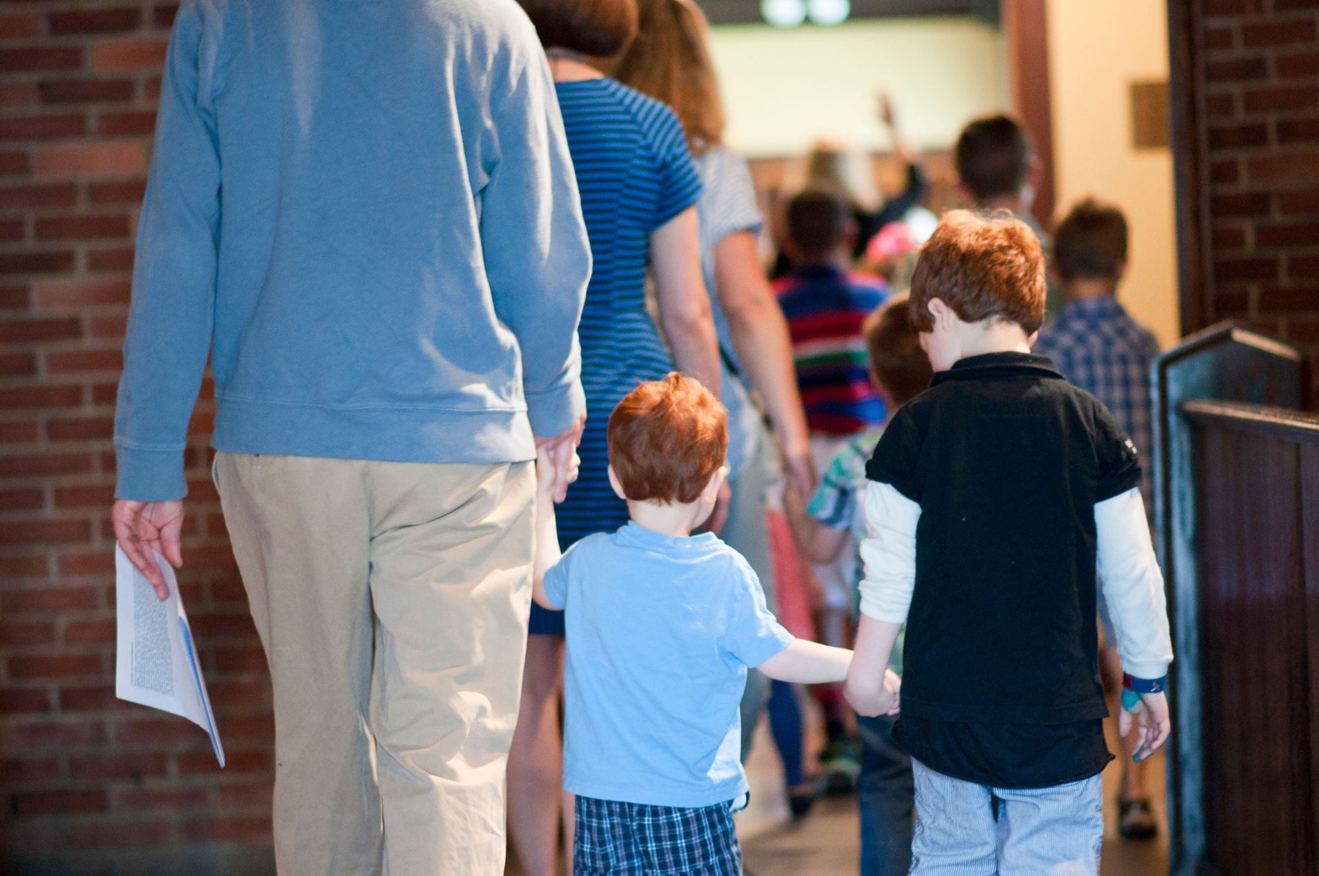 Photographed from behind, a father and two red-headed children holding hands at Parish of the Epiphany