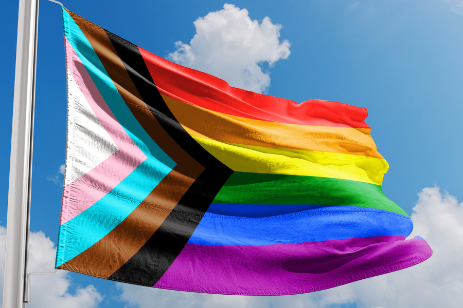 A Pride flag with a blue sky behind